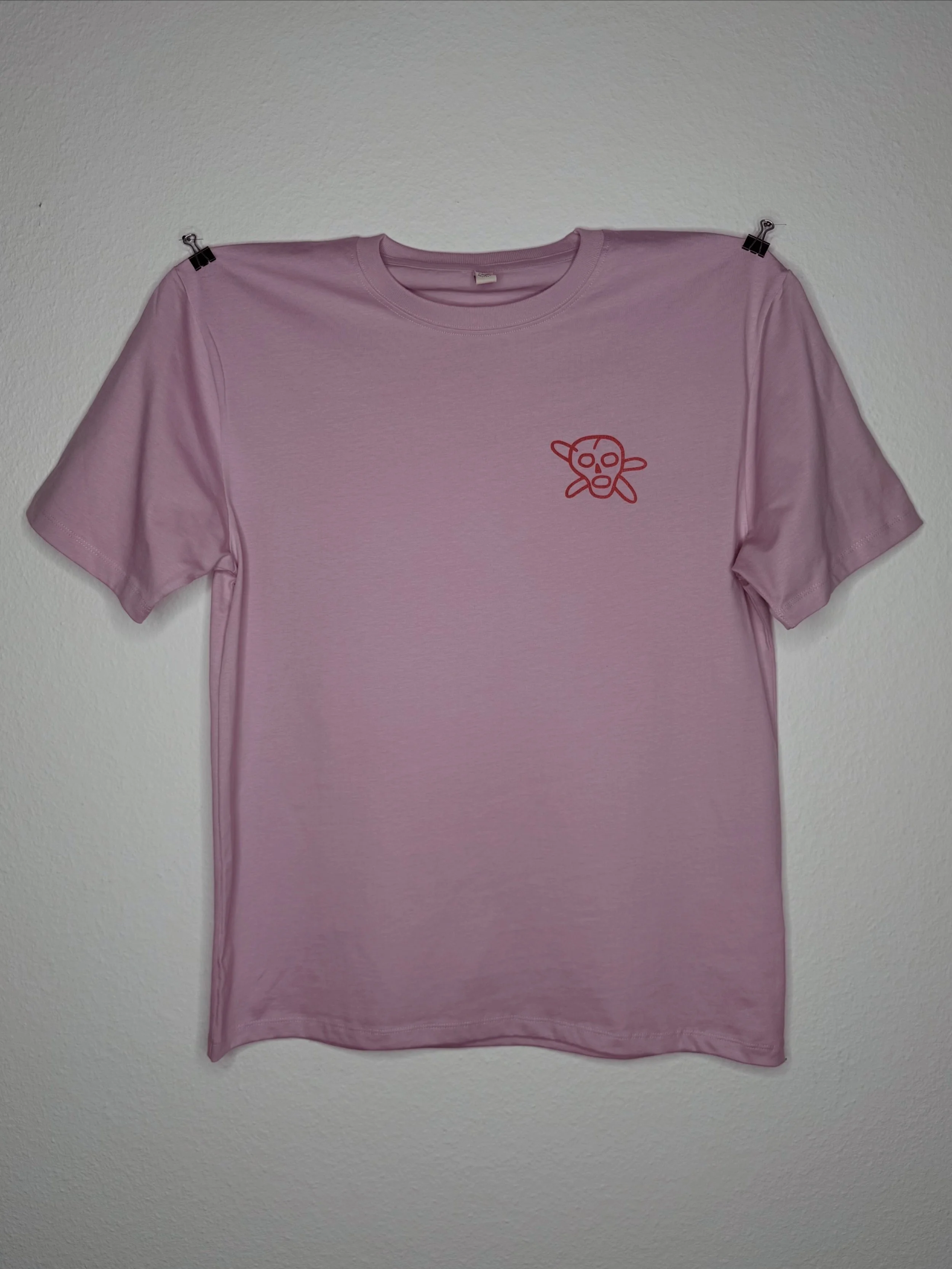 Rosa T-Shirt mit Rundhalsausschnitt und kleinem rotem Cartoon-Aufdruck, an einer Wand befestigt