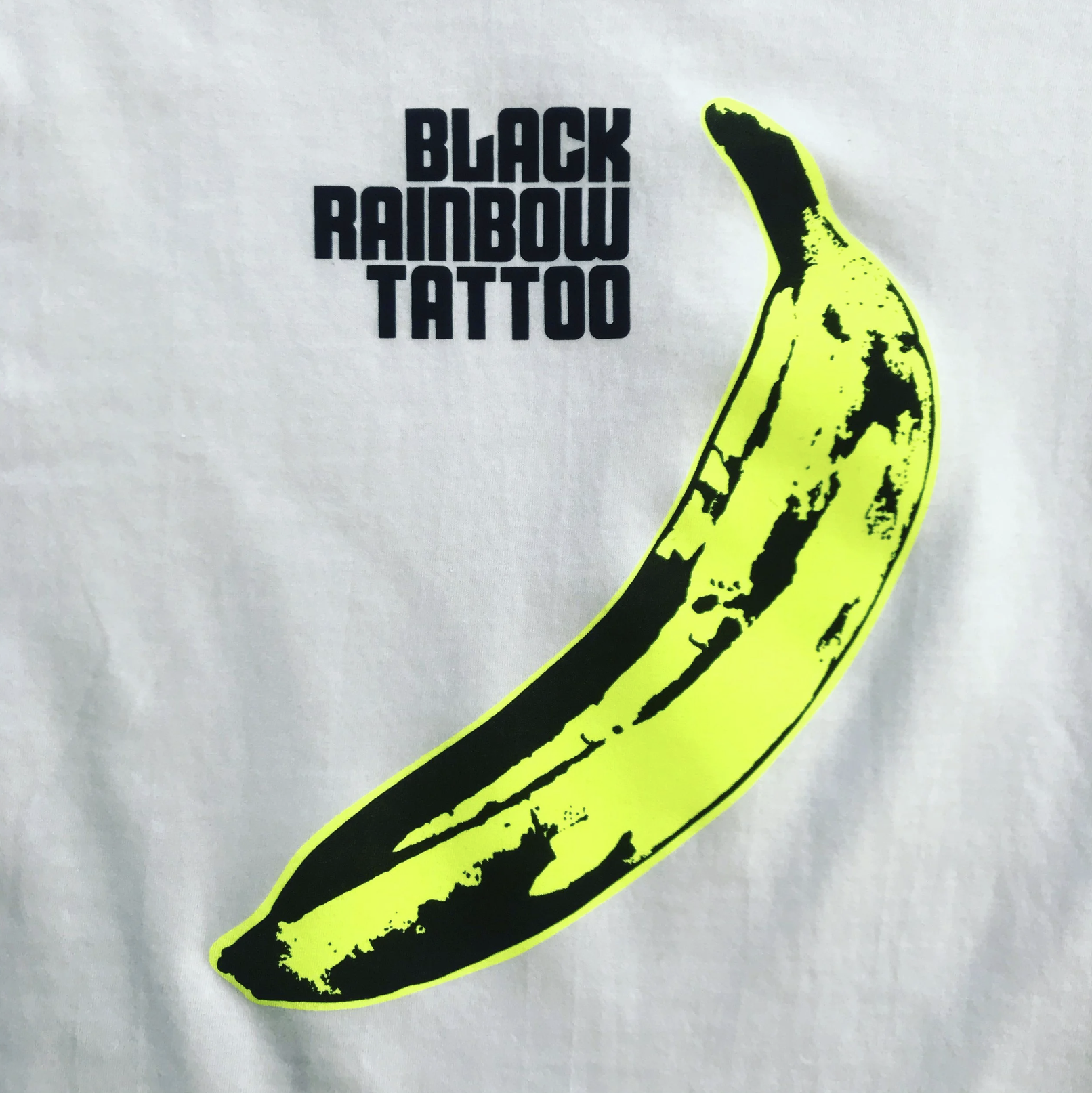 Neongrüne Banane mit schwarzer Grafik neben dem Schriftzug „BLACK RAINBOW TATTOO“.