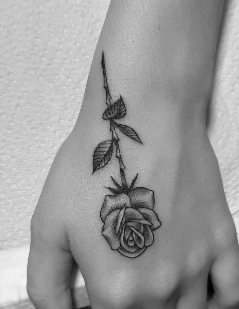 Schwarz-weißes Rosentattoo mit Blättern auf dem Handrücken
