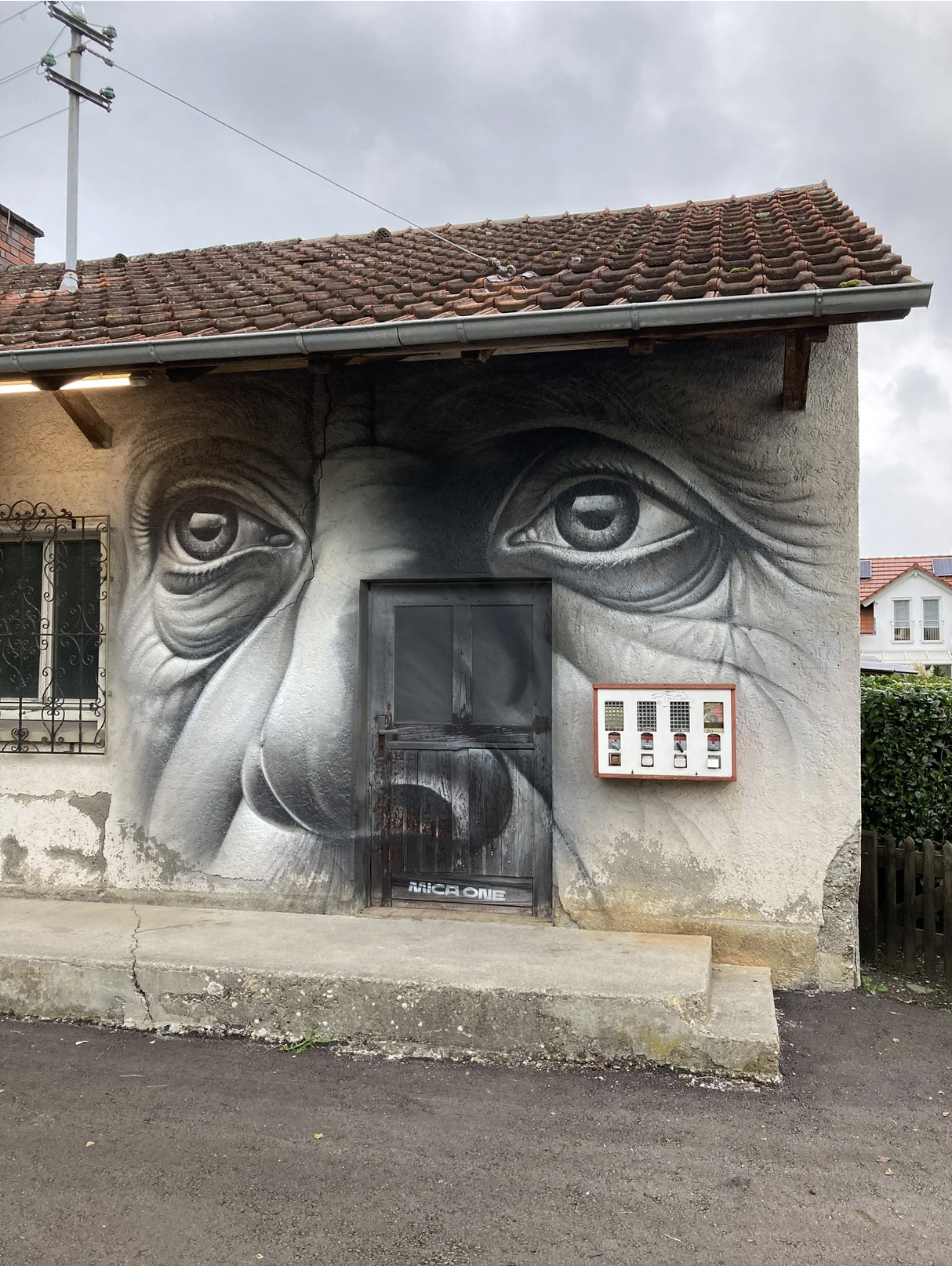Graffiti eines Gesichts, das den Eingangsbereich eines Gebäudes bedeckt, mit großen, realistischen Augen und einer Nase, in Schwarz, Weiß und Grau.