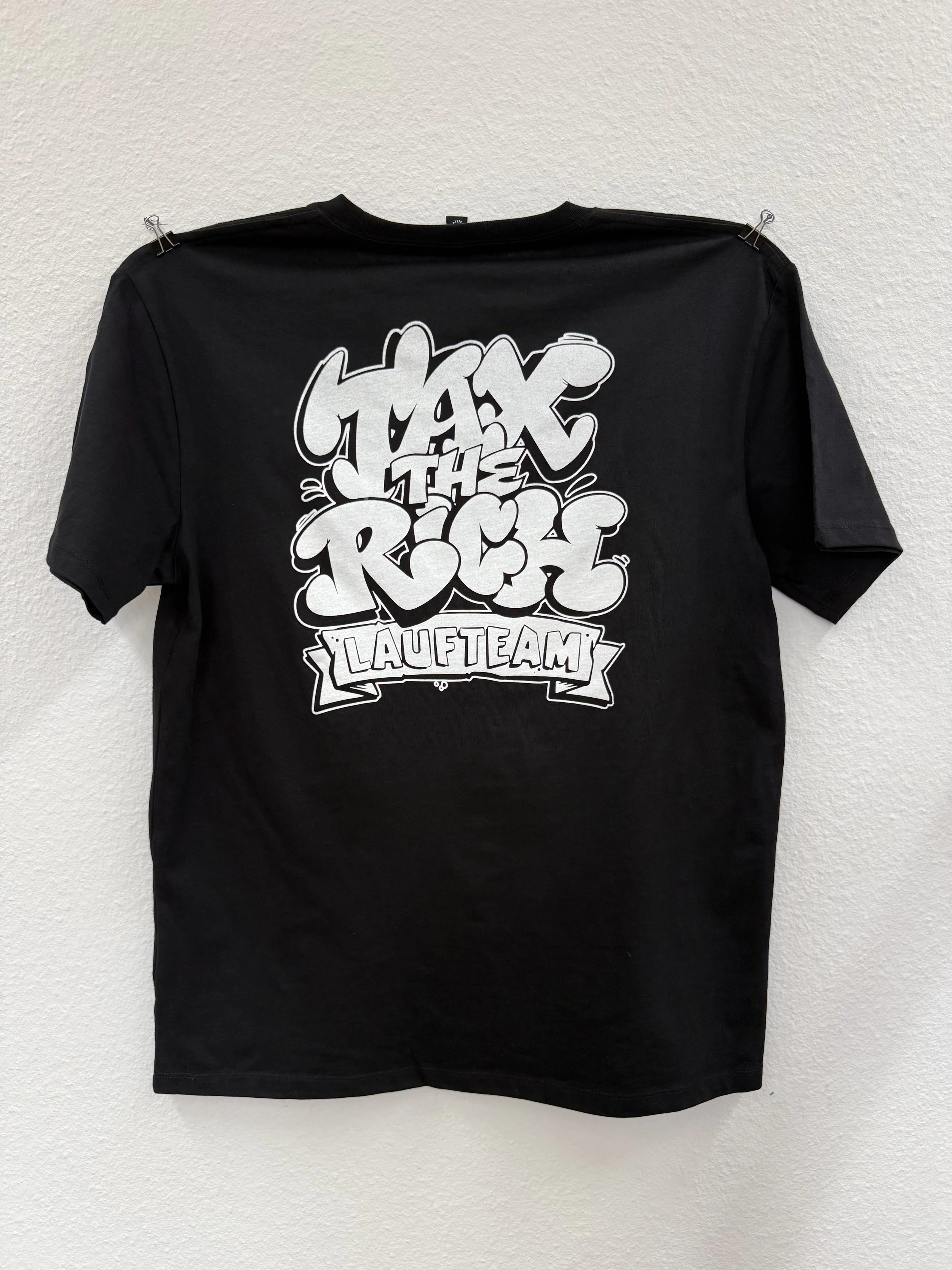 Schwarzes T-Shirt mit weißem Graffiti-Aufdruck „TAX THE RICH“ und Banner „LAUFTEAM“