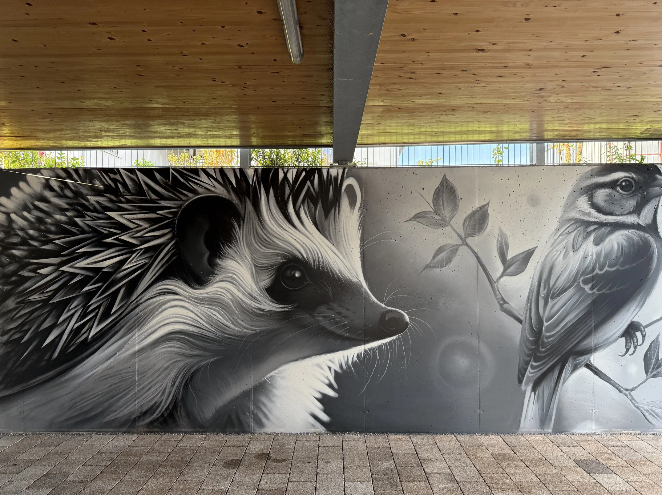 Wand mit Graffiti-Kunst eines Tieres, das wie ein Löwe aussieht, mit schwarzen und weißen Farbmustern und Pflanzenmotiven.