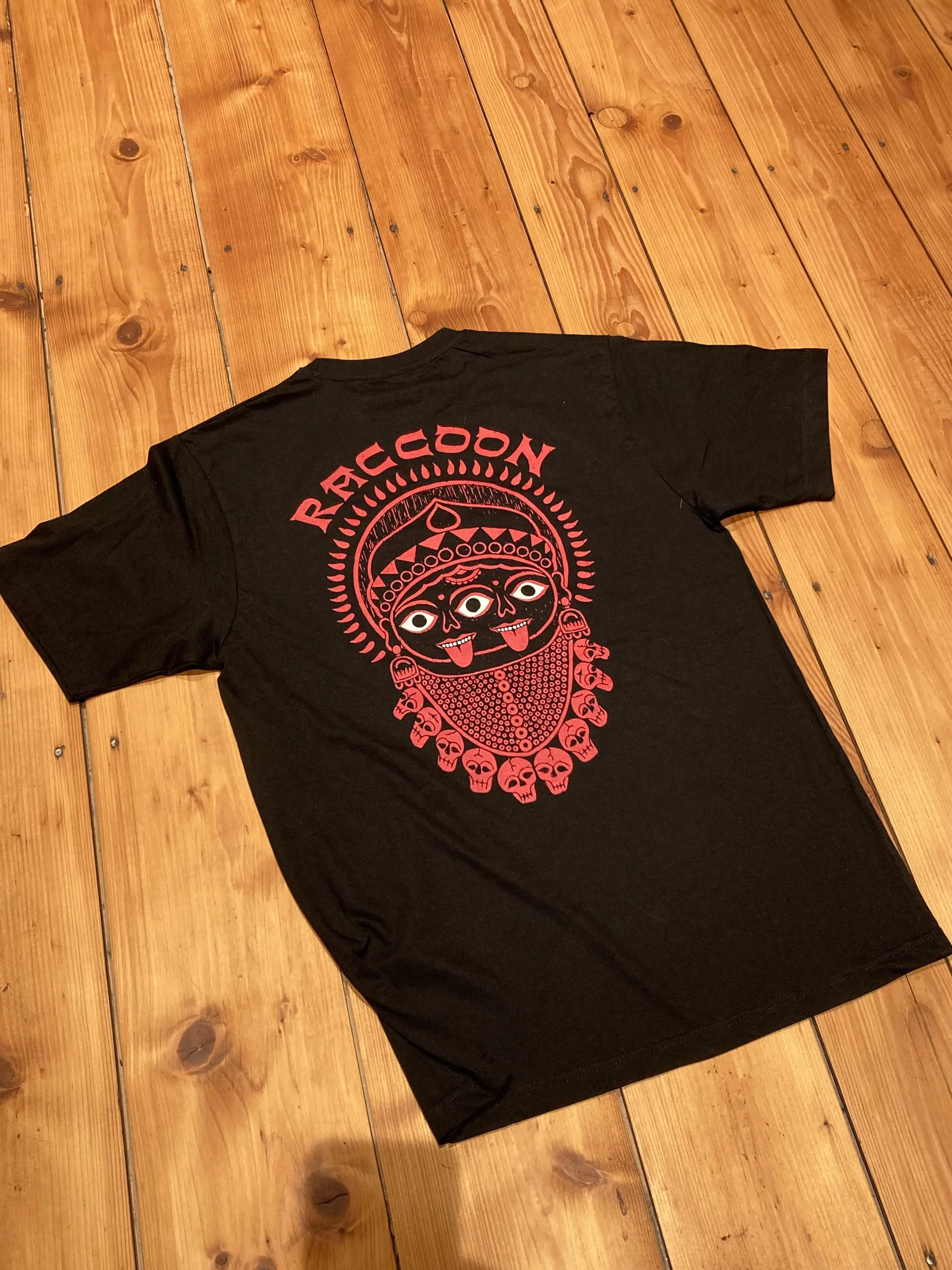 Schwarzes T-Shirt mit rotem Kali-Göttin-Aufdruck auf einem Holzboden