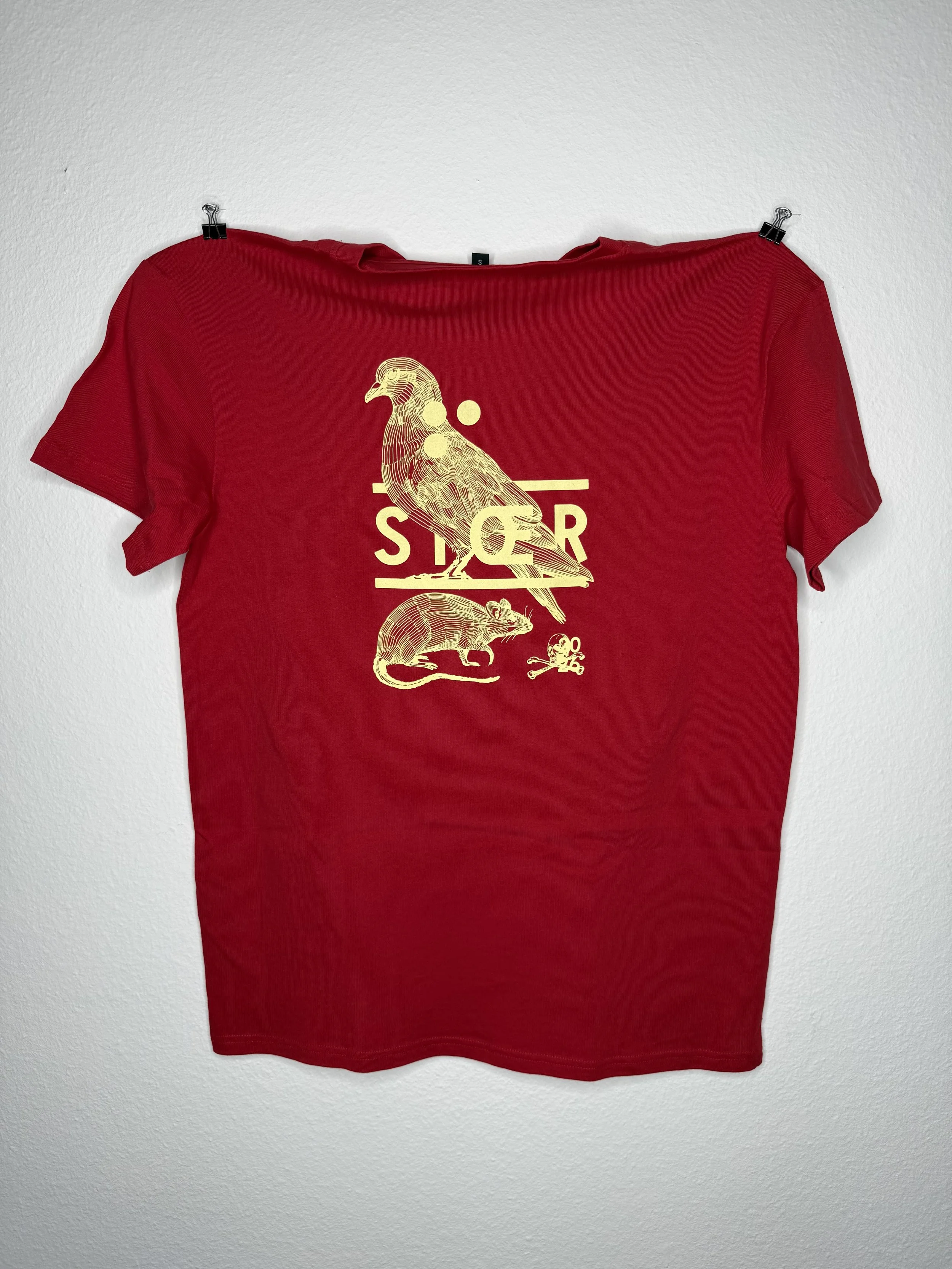 Rotes T-Shirt mit goldfarbenem Vogel-, Ratten- und Schriftzug-Print, an einer weißen Wand befestigt