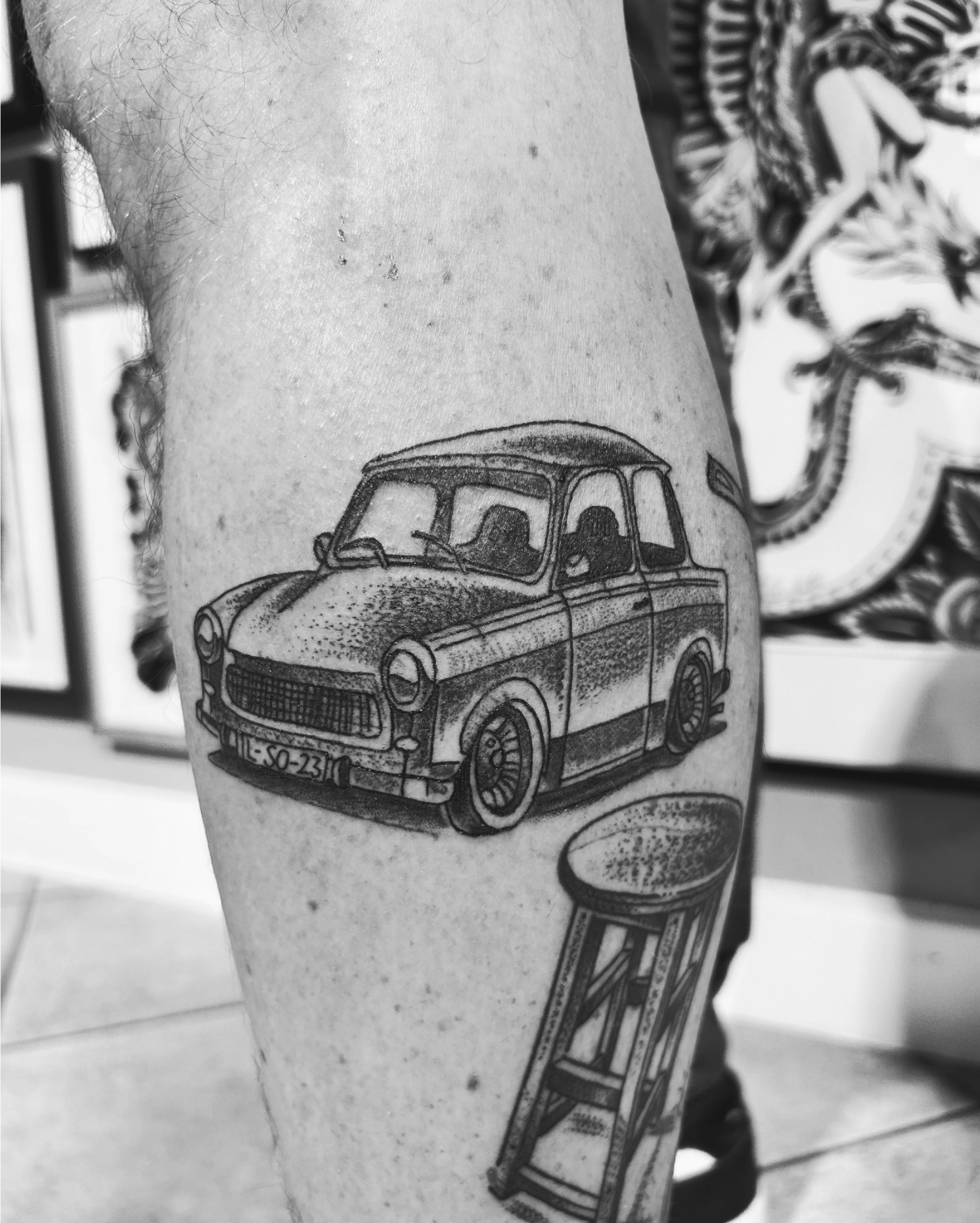 Schwarz-Weiß-Nahaufnahme eines Tattoos mit einem gezeichneten Oldtimer auf einem Bein