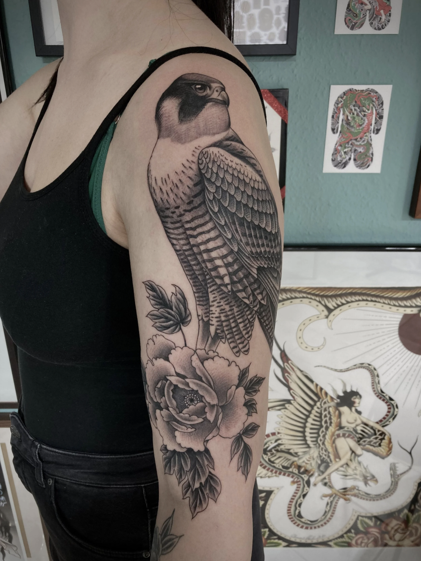 Detailaufnahme eines großflächigen Schwarzgrau-Tattoos mit Vogel und Blüten auf dem Oberarm einer Person