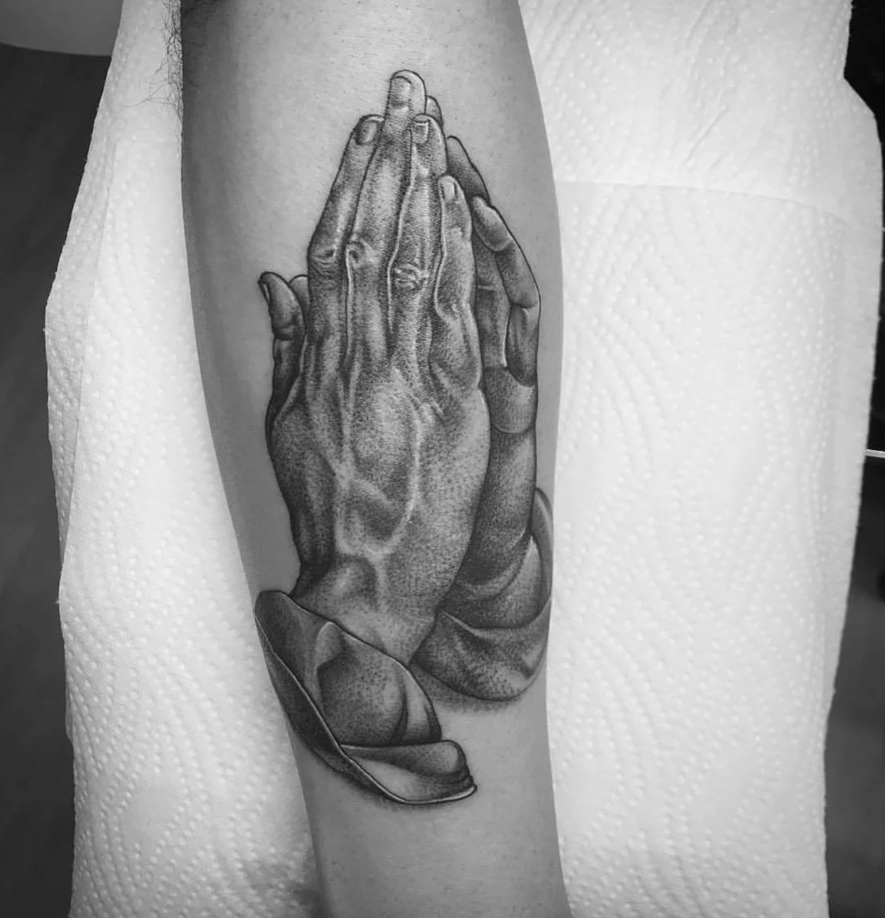 Schwarz-weißes Tattoo betender Hände mit Rosen und Blättern auf dem Unterarm