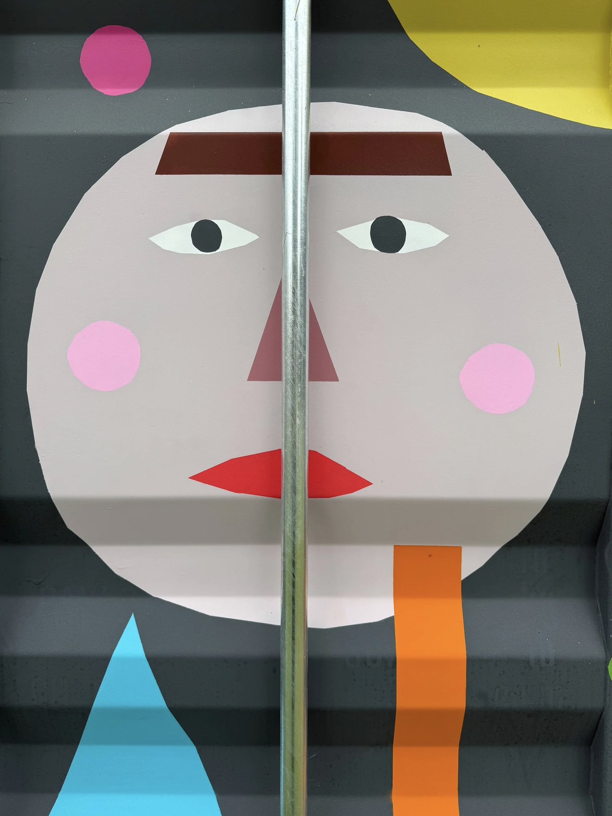 Abstrakte, geometrische Darstellung eines Gesichts mit einfarbigen Flächen. Das Gesicht ist rund mit schwarzen Augen, rosa Wangen, roten Lippen, brauen Augenbrauen und einer roten Nase. Es gibt bunte Elemente wie eine blaue Dreiecksform und eine oran