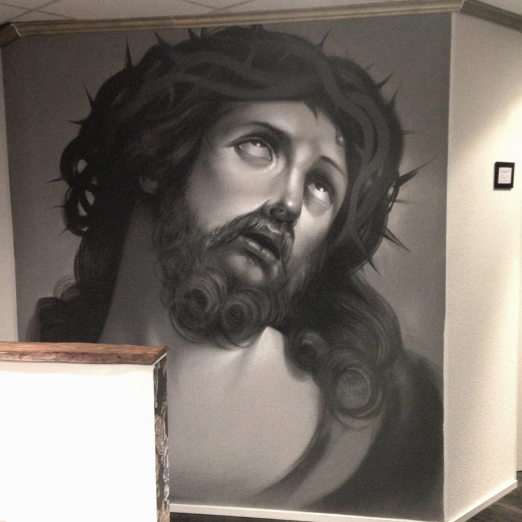 Schwarz-weiß Wandbild eines Jesus Christus mit Dornenkrone, Blick nach oben, im Kunststil.