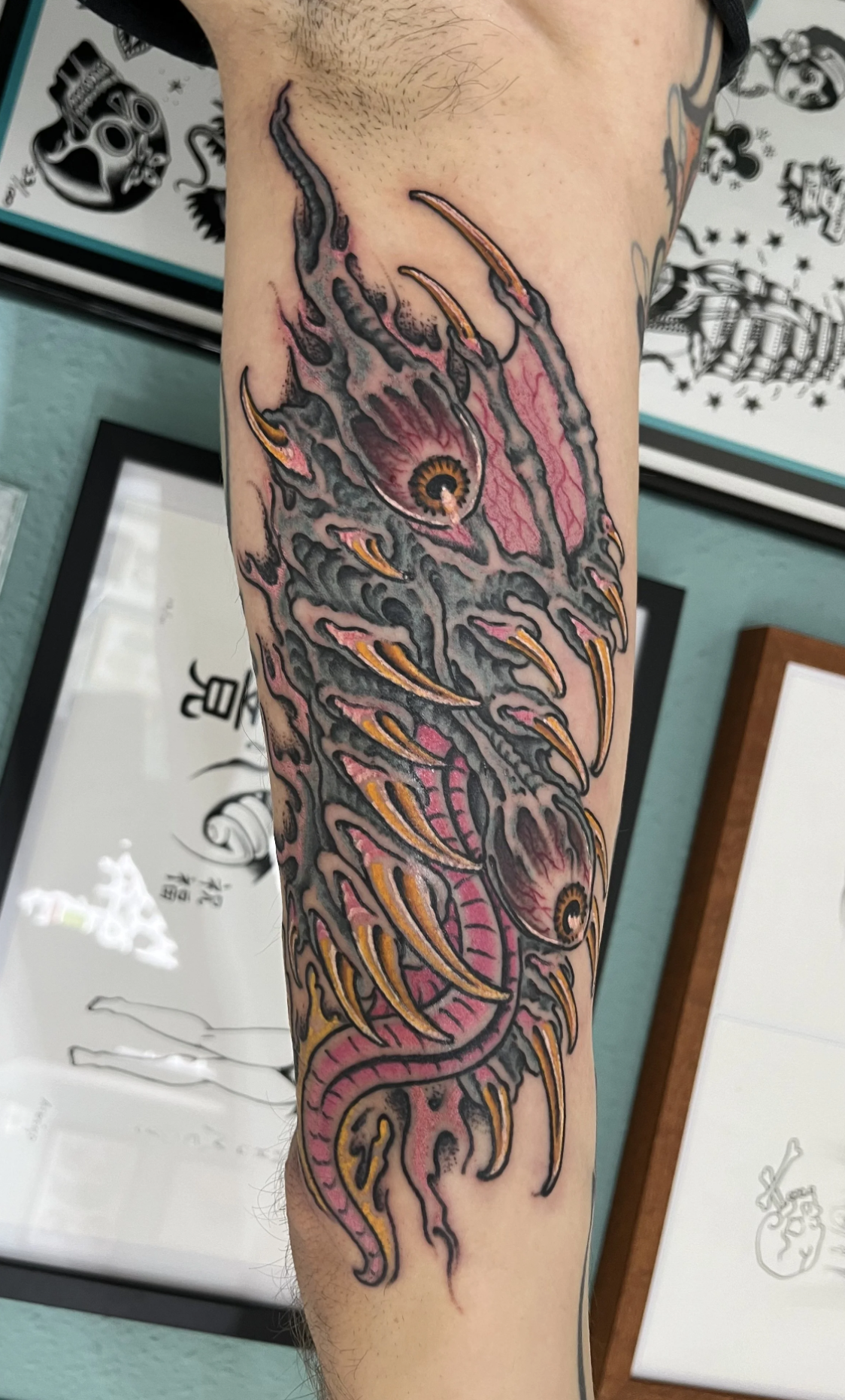 Nahaufnahme eines farbenfrohen Unterarm-Tattoos mit einem stilisierten Drachen in Rosa, Grau und Orange.