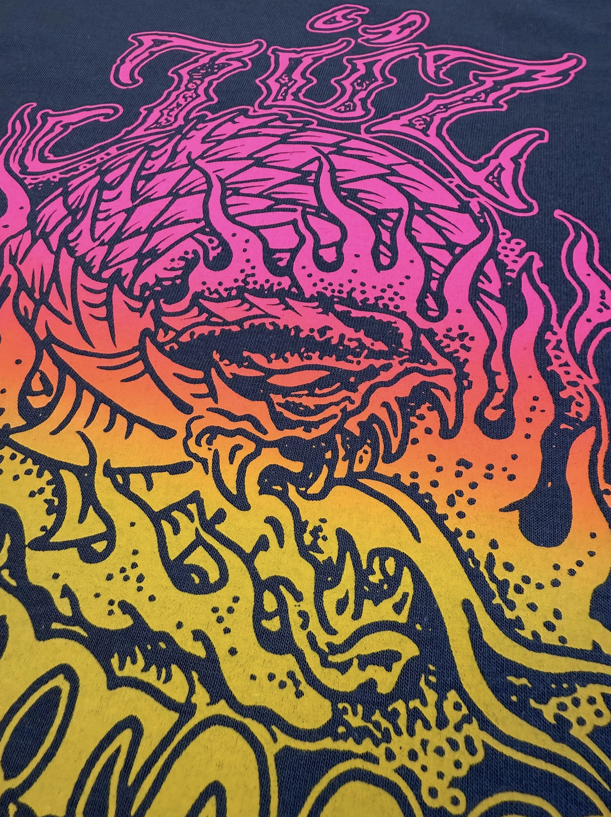 Nahaufnahme eines farbenfrohen Gothic-T-Shirts mit Totenkopf- und Dämonenmotiv in Pink, Orange und Gelb