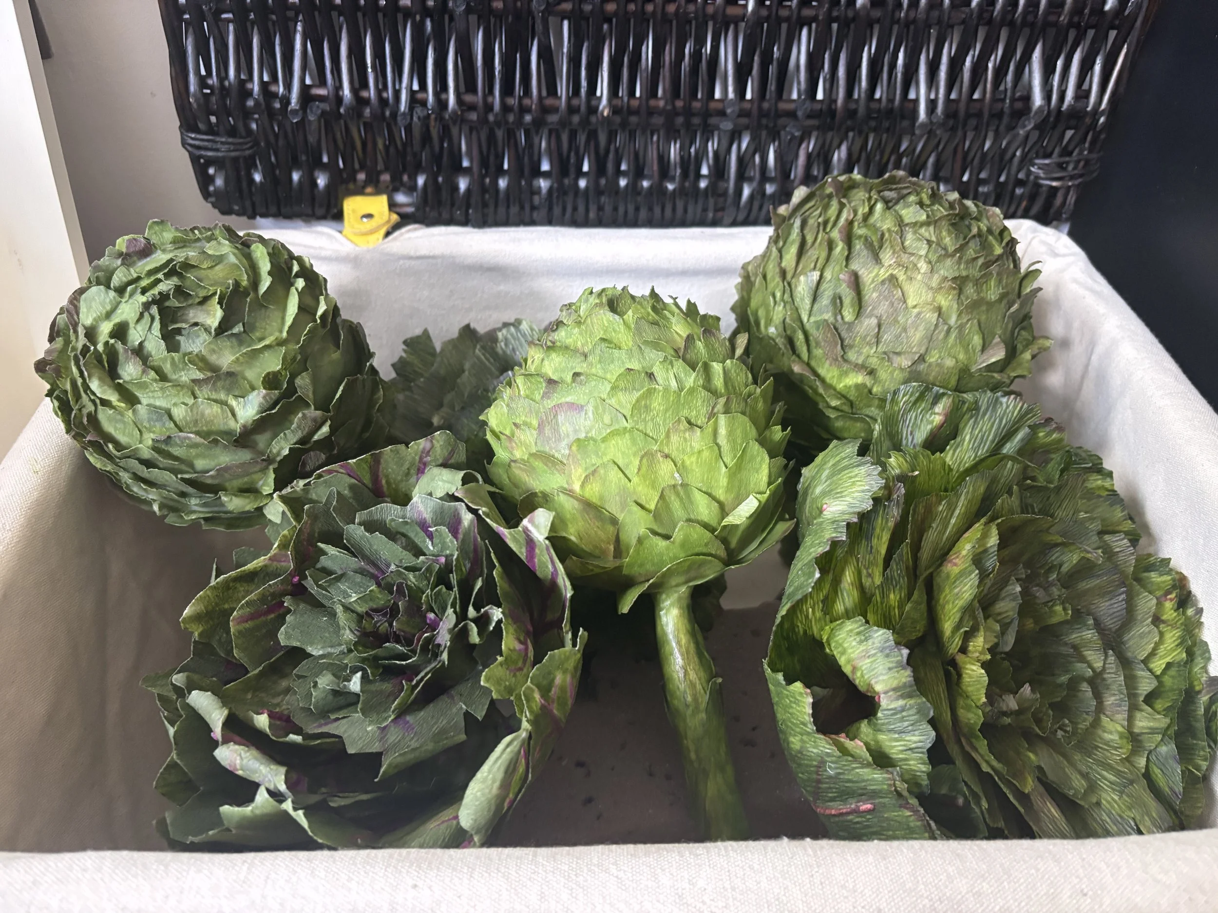 Close-up of green artichokes with purple-tinged leaves on a white cloth surface