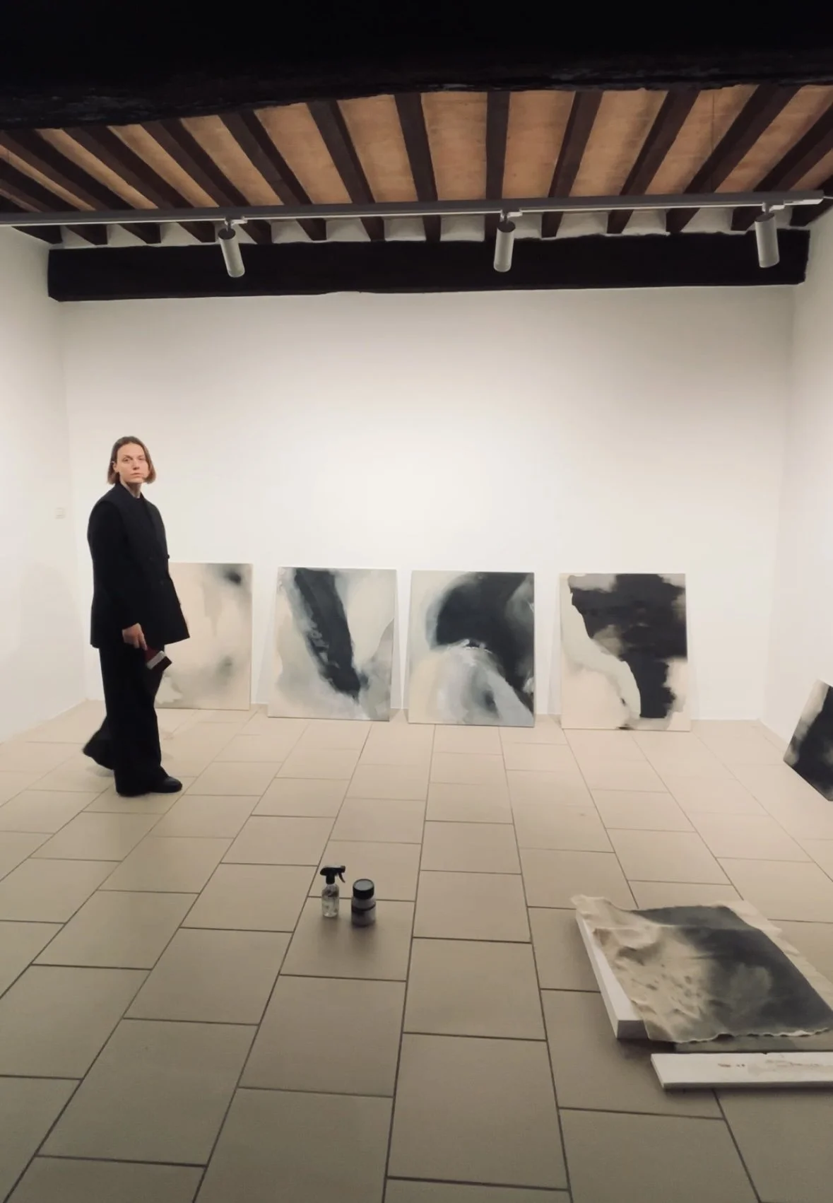 Woman standing in a gallery beside abstract black-and-white paintings displayed against a white wall.
