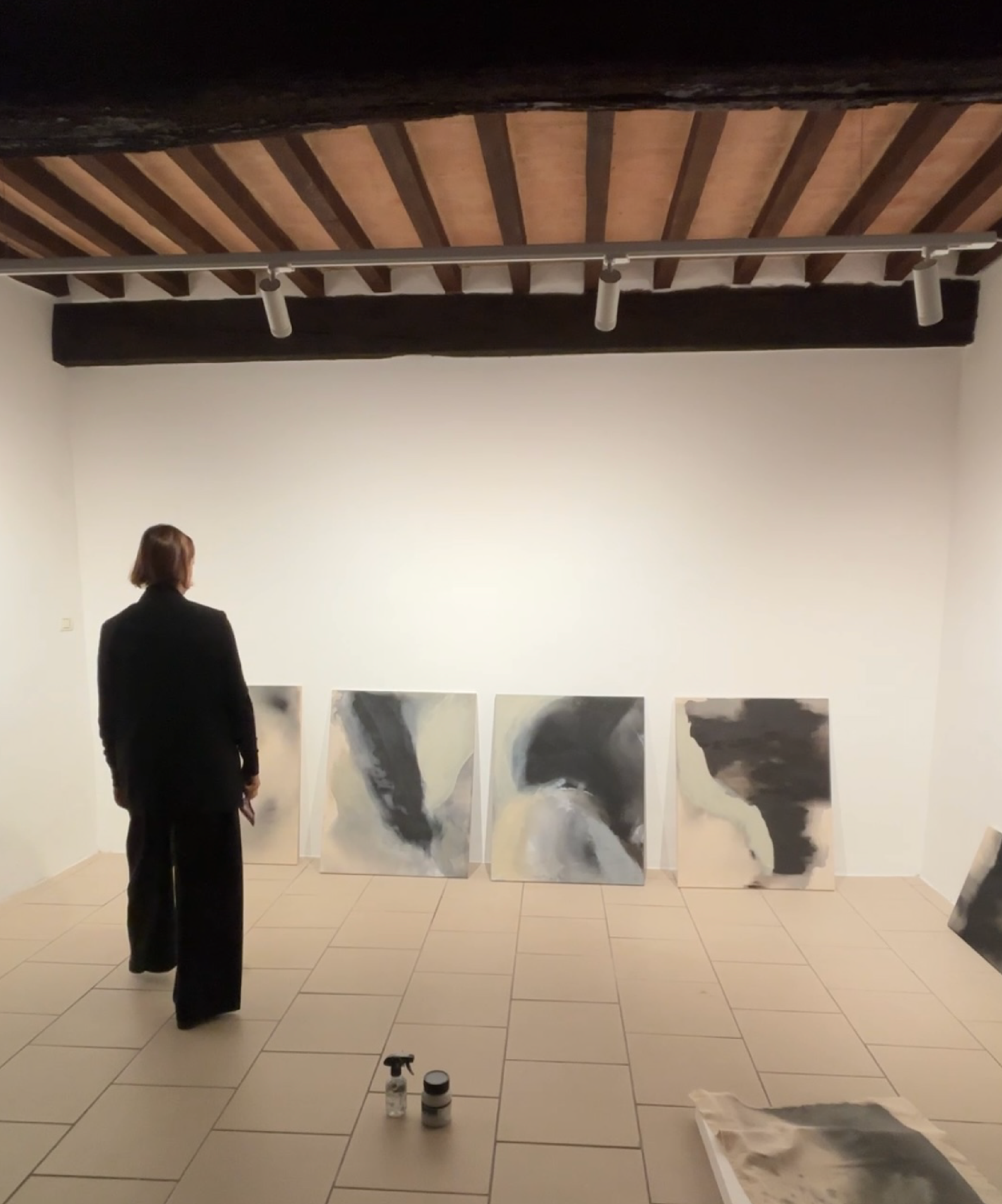 Person viewing abstract paintings in a contemporary art gallery with exposed wooden beams and track lighting