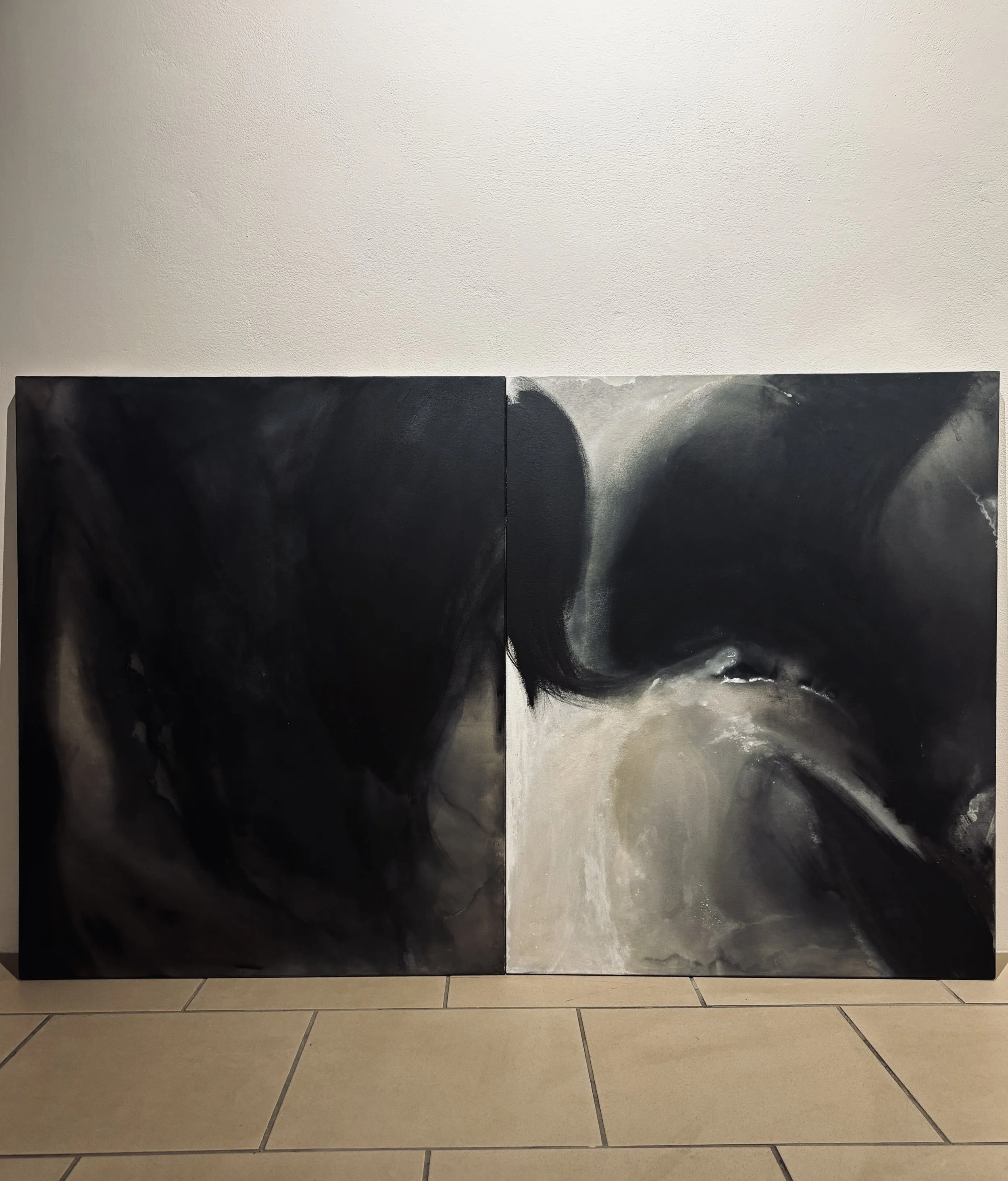 Two large dark abstract paintings leaning against a textured white wall above a tiled floor.