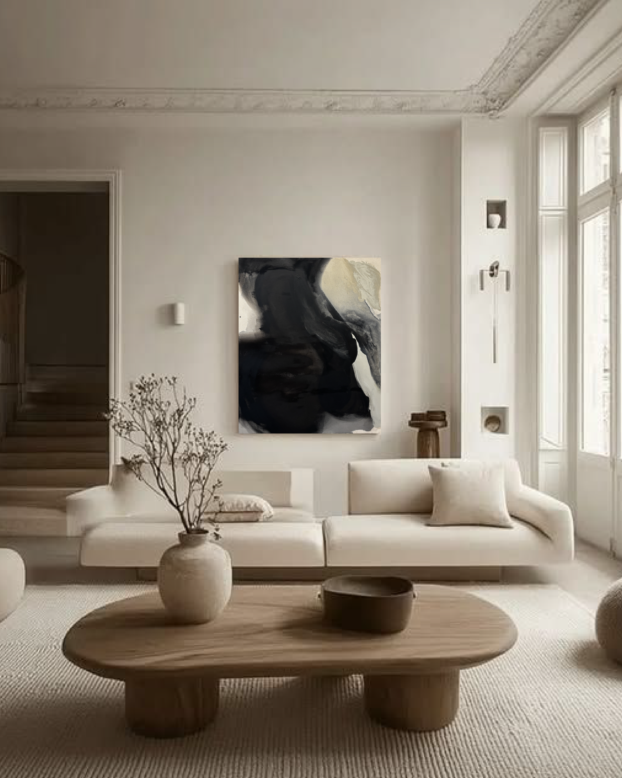 Bright modern living room with white sofas, abstract black-and-white wall art, large windows, staircase, decorative vase, and wooden coffee table.