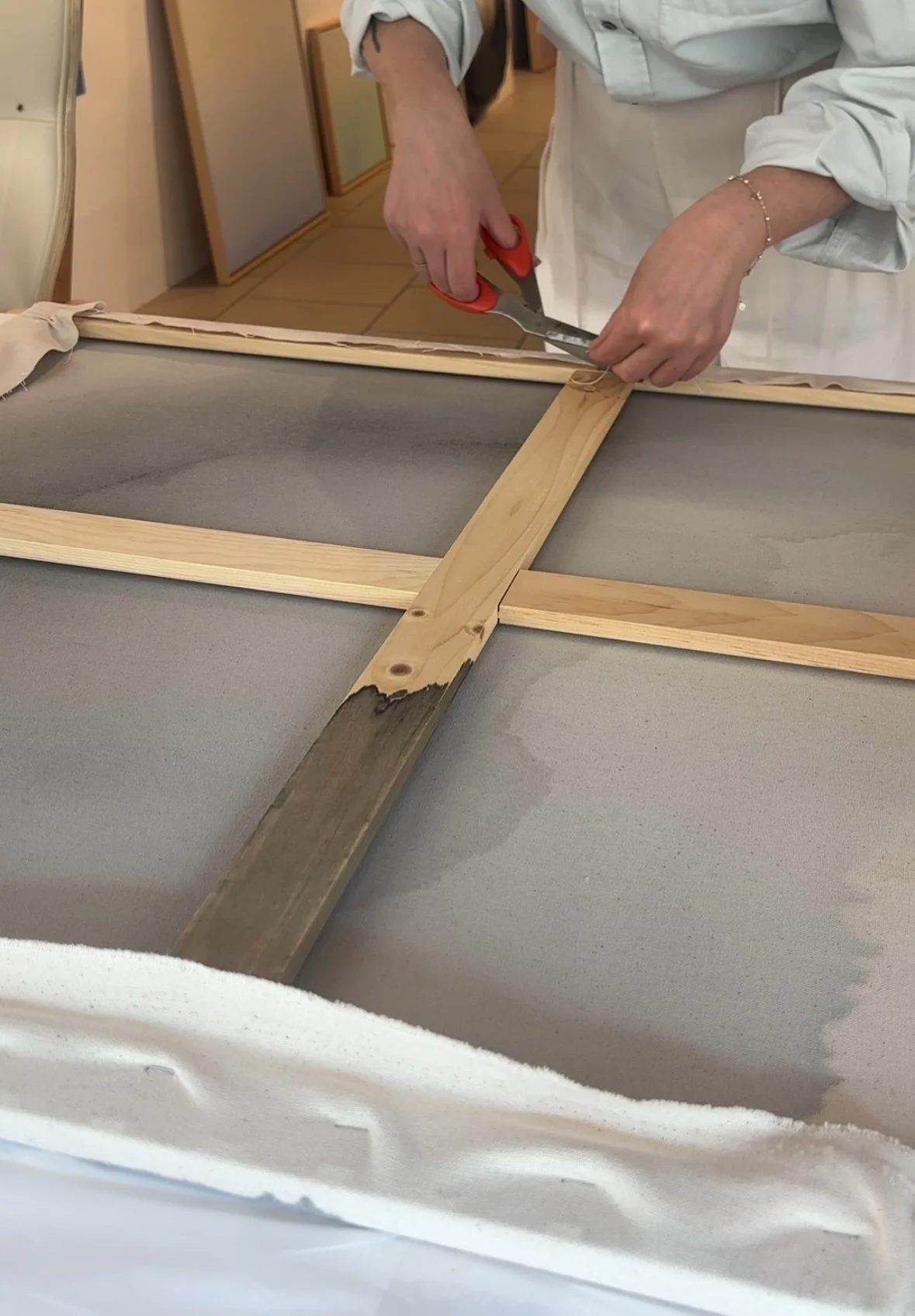 Person cutting fabric with scissors from a wooden picture frame on a work surface
