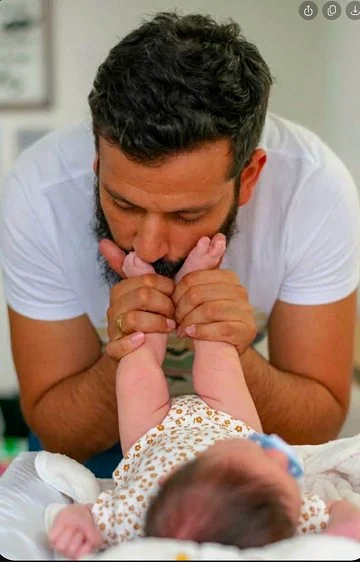A man gently kissing a baby's hand in a hospital setting.