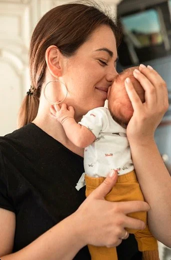 A woman holding a newborn baby close to her face, smiling softly while the baby is touching her nose.