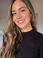 Close-up of a young woman with long wavy hair, smiling, wearing a black top.