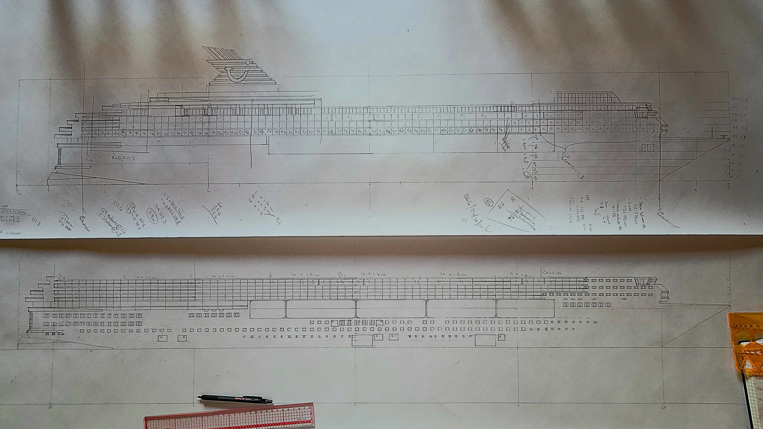 Blueprint of a large ship, including various sections, measurements, and technical notations, with a pen and a ruler on the table.