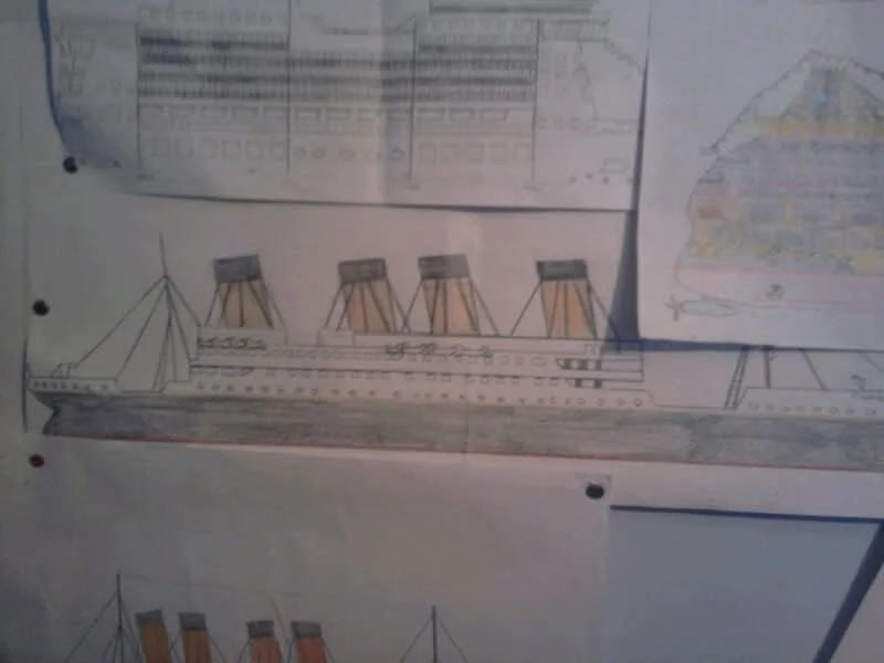 Drawing of RMS Titanic with four smokestacks and a detailed deck, pinned to a wall among other sketches and plans.