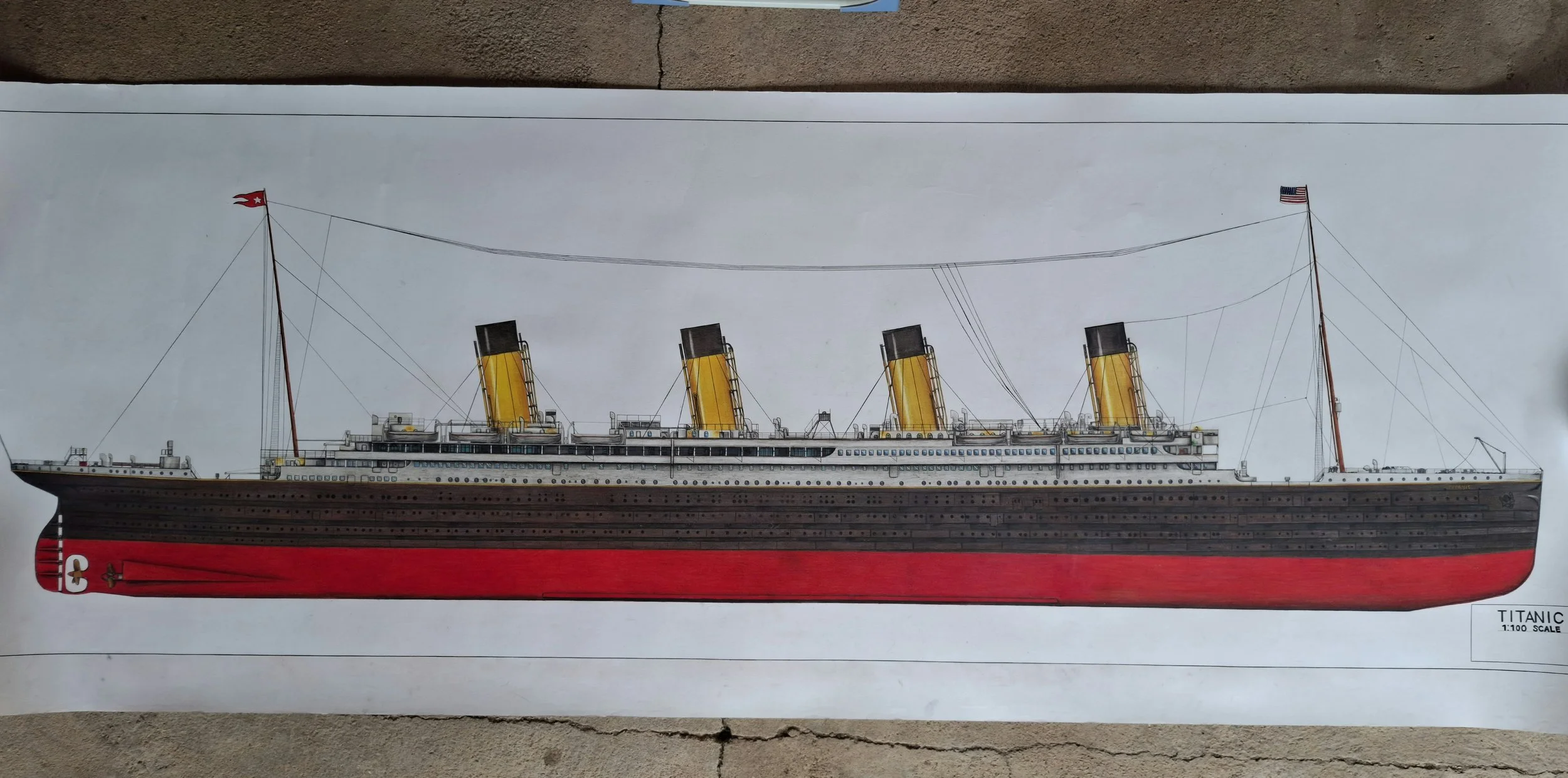 A detailed diagram of the Titanic ship model, showing its four large yellow funnels, multiple decks, and flags at each end, with a label indicating a 1:100 scale.