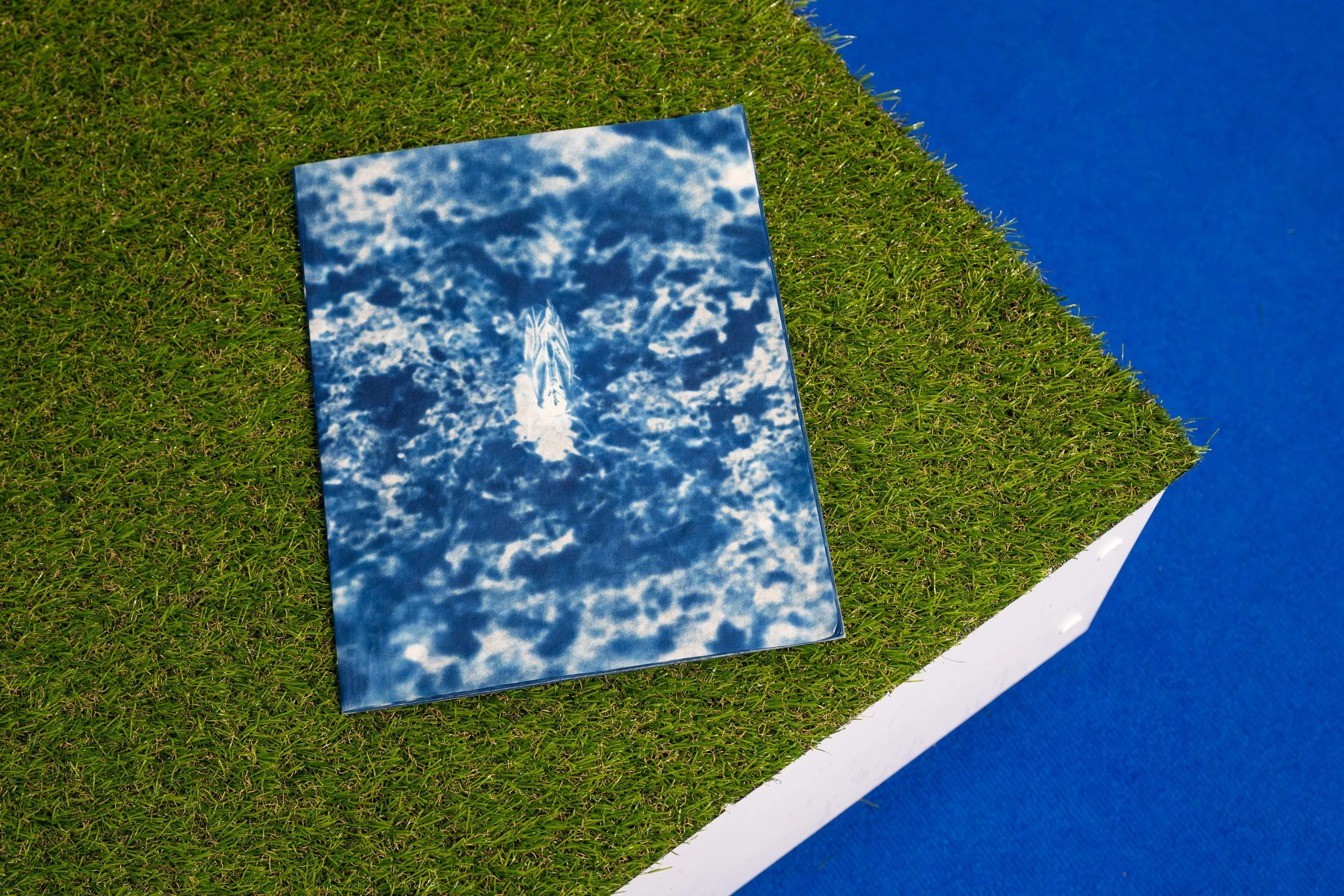 A mirrored surface reflecting a blue sky with white clouds, placed on green grass with a blue background.