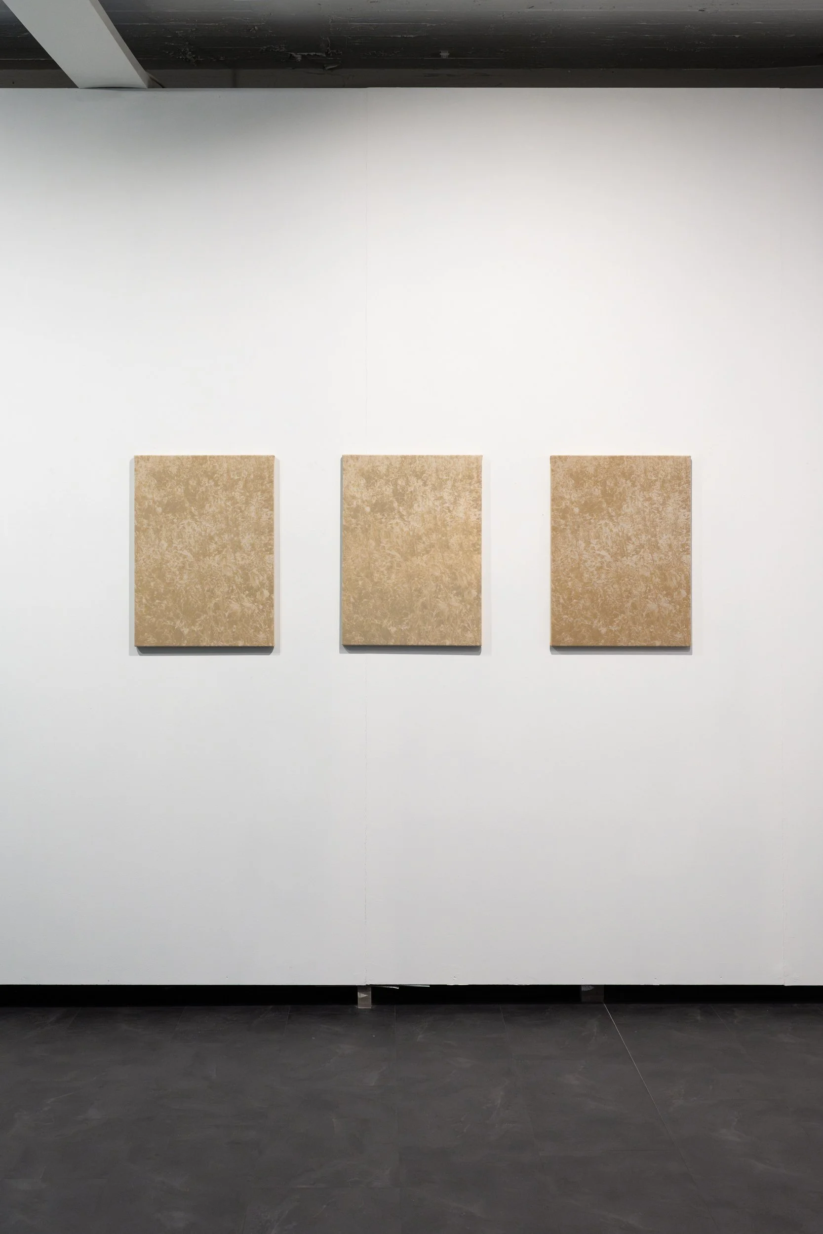 Three beige textured art panels are hung evenly spaced on a white gallery wall, with a dark grey floor below.