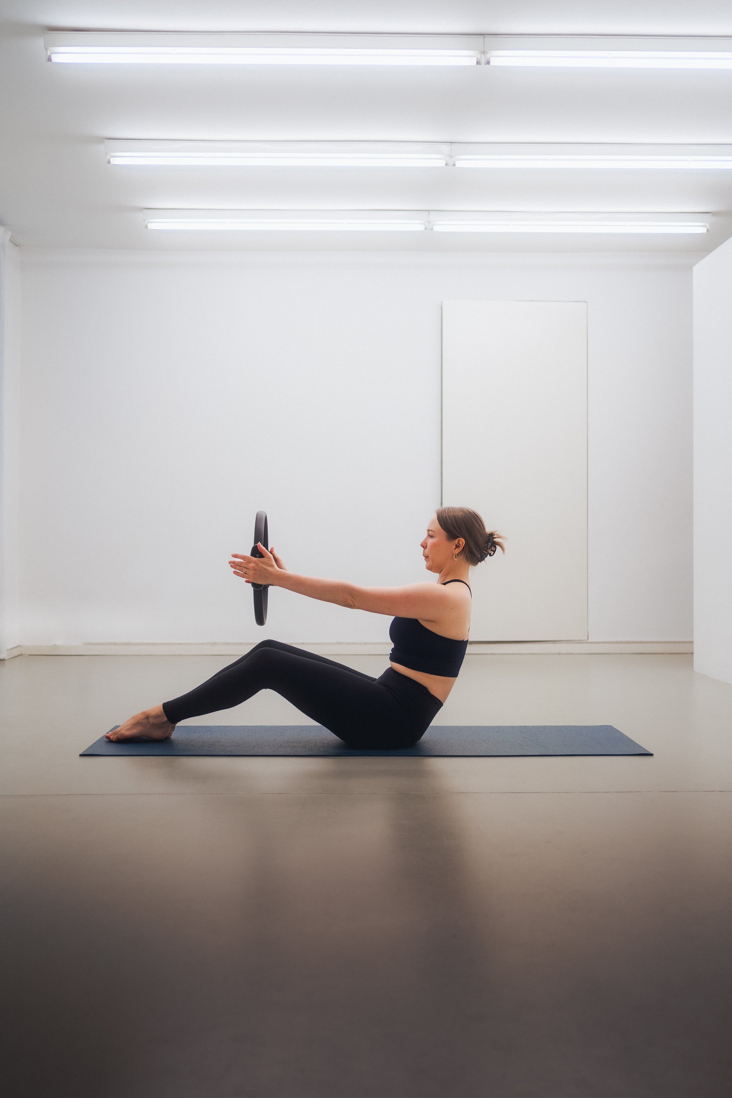 Woman performing a Pilates exercise while holding a fitness ring on a yoga mat