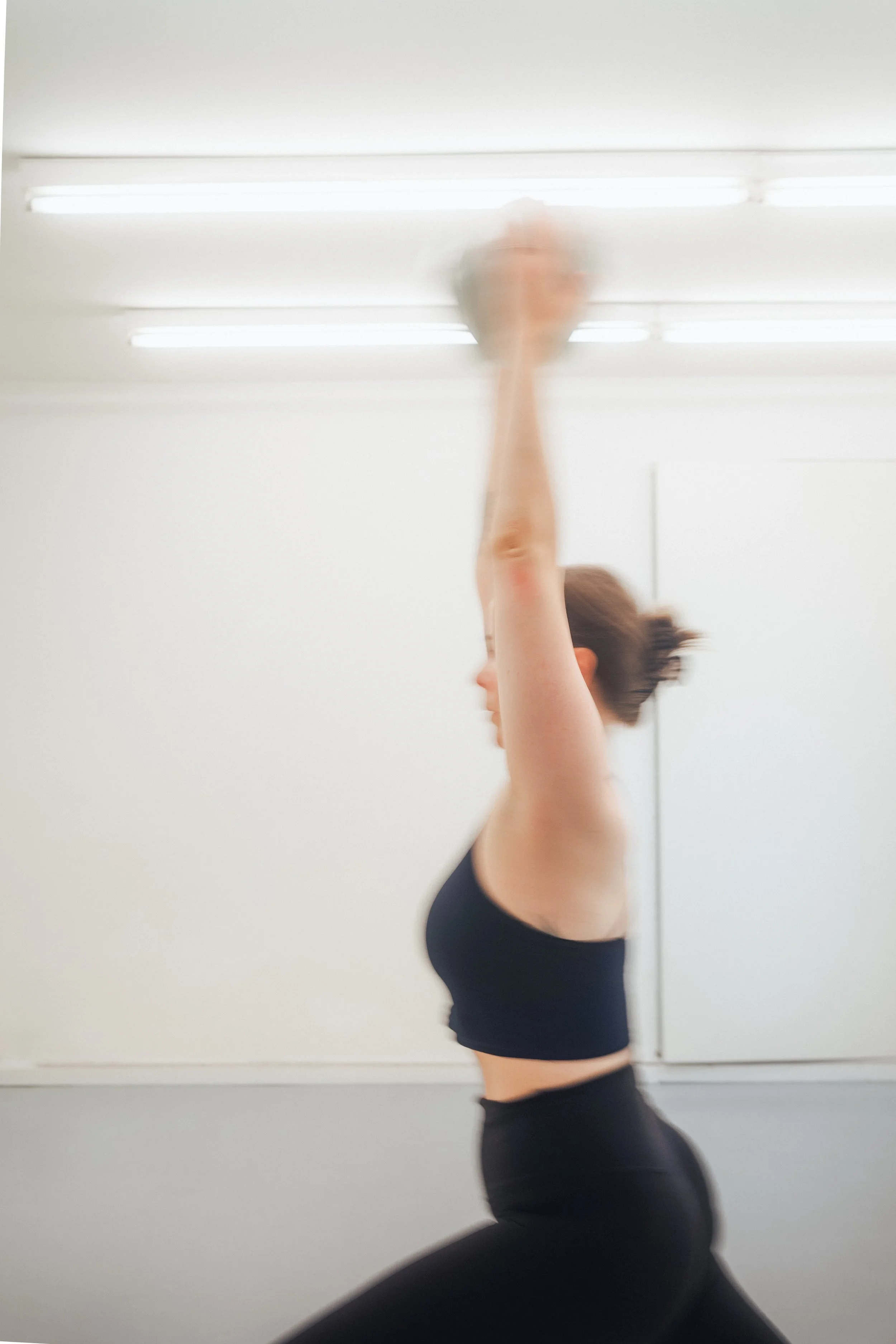 Woman in black workout clothes stretching her arm in front of a bright window