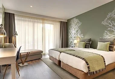 Modern bedroom with two twin beds, green accent wall, white tree mural, and floor-to-ceiling windows