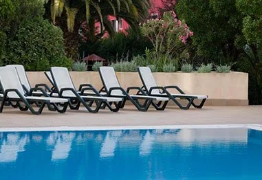 Outdoor swimming pool with empty lounge chairs and lush tropical landscaping