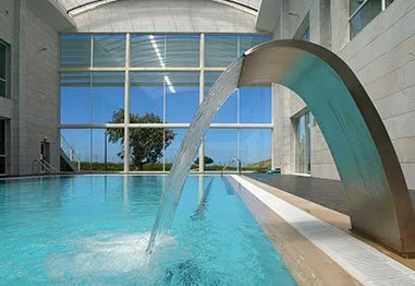 Indoor swimming pool with a large curved metal water feature pouring into turquoise water