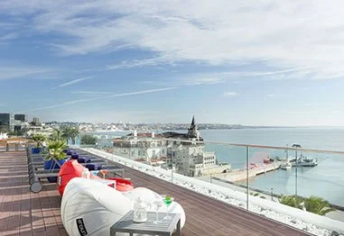 Seaside rooftop terrace overlooking a marina, pier, and coastal city under a blue sky