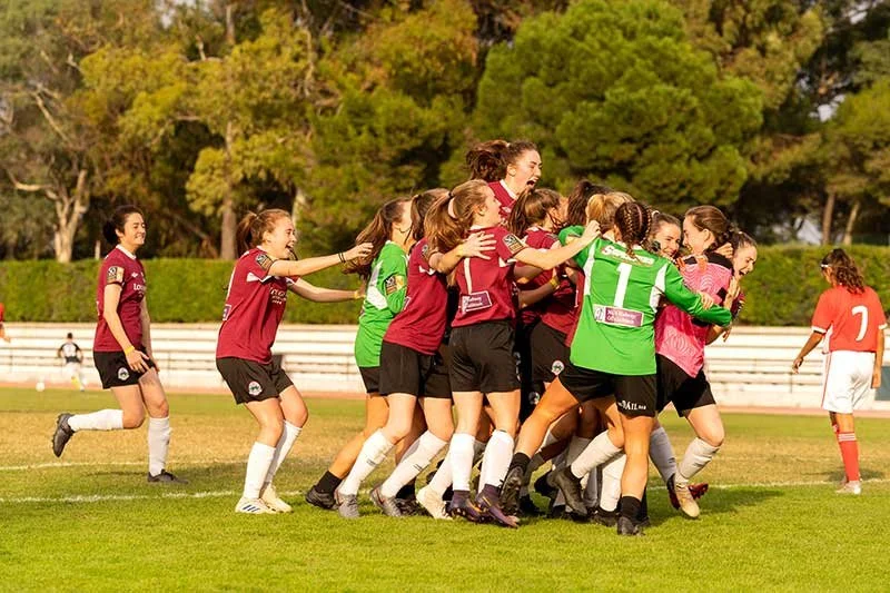 Women's soccer team celebrating together on a sunny outdoor field
