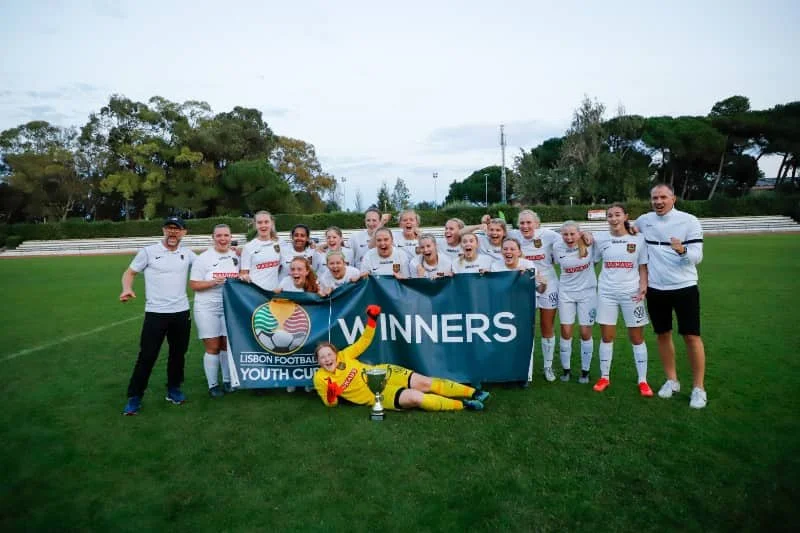 Youth soccer team posing with a WINNERS banner and trophy on a grassy field