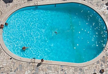 Aerial view of swimmers in a bright blue outdoor swimming pool surrounded by stone decking