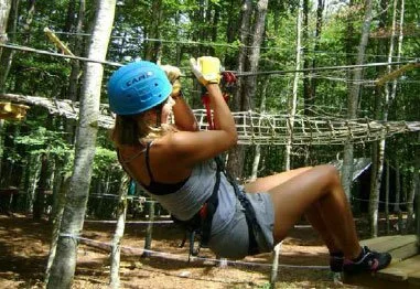 Woman wearing a blue helmet navigating a forest ropes course obstacle.