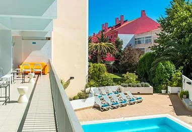 Hotel courtyard with swimming pool, lounge chairs, landscaped gardens, and a sunny balcony patio