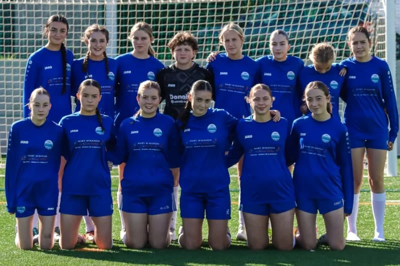 Girls' soccer team posing in blue uniforms in front of a goal net