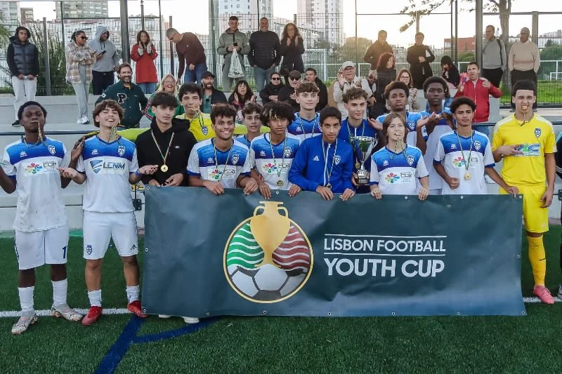 Youth soccer team posing with medals and a trophy behind a Lisbon Football Youth Cup banner