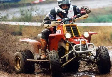 Rider in protective gear driving a red sport quad ATV through muddy terrain