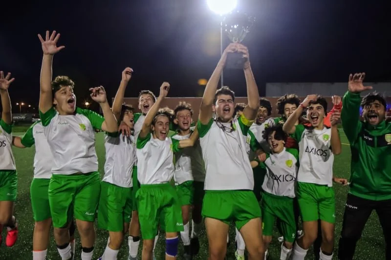 Joyful youth soccer team in green and white uniforms celebrating a championship victory on the field at night, holding a trophy overhead