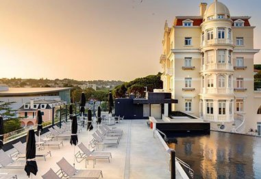 Luxury waterfront hotel with a domed tower, outdoor terrace seating, and calm reflecting pool at sunset