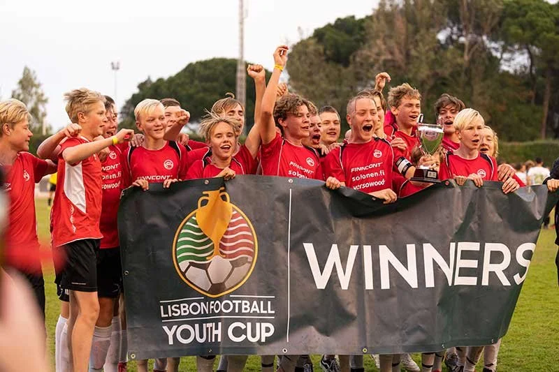 Youth soccer team celebrating a Lisbon Football Youth Cup win behind a winners banner