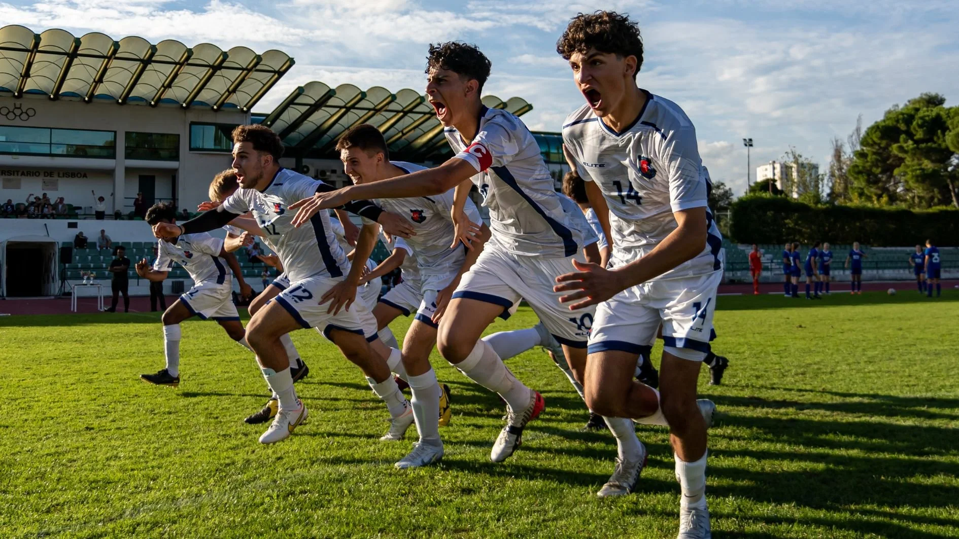 Excited soccer players in white uniforms sprinting across a field after scoring at a stadium