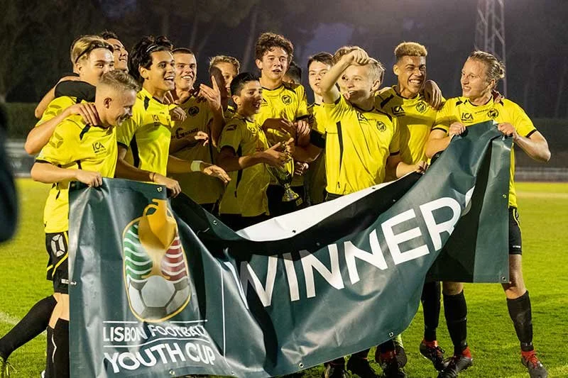 Youth soccer team in yellow jerseys celebrating with a Lisbon Football Youth Cup winner banner