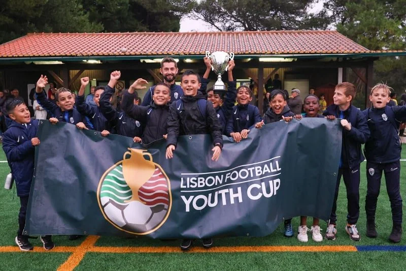 Youth soccer team celebrating with a trophy behind a Lisbon Football Youth Cup banner