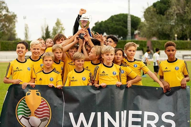 Youth soccer team in yellow jerseys celebrating with a trophy behind a winners banner